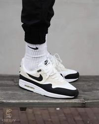 Nike Air Max 1 Essential White Pure Platinum Black – close-up van Swoosh in zwart leer, grijze panelen en witte mesh upper