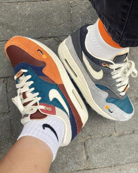 In-hand shot van Nike Air Max 1 Kasina Won-Ang Orange DQ8475-800 – textuur van suède en details zoals het Won-Ang logo en reflectieve elementen