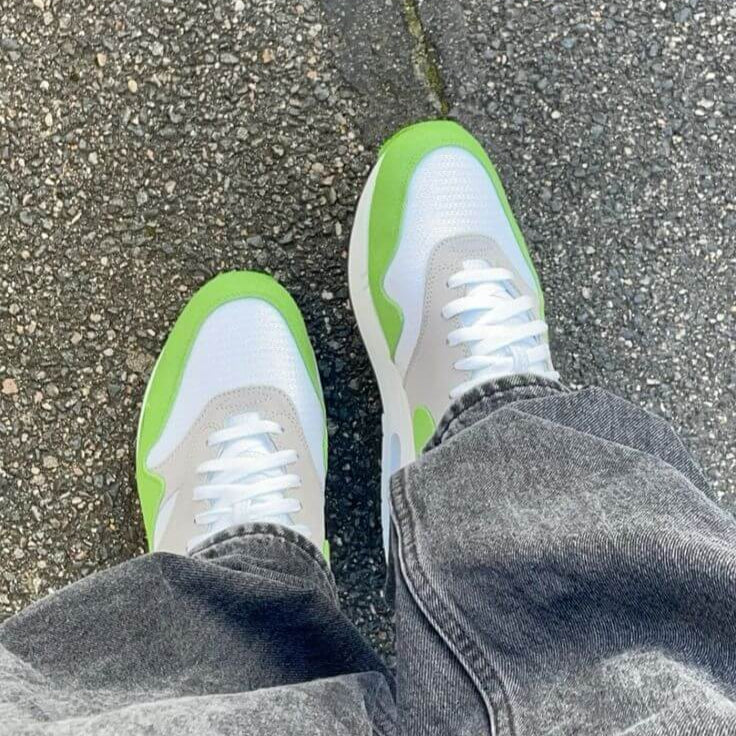 Top-down foto van het paar gedragen op straat, waarbij het Chlorophyll-groen afsteekt tegen grijze denim en asfalt