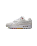 Zijaanzicht van de Air Max 1 met pom pom-details, witte canvas upper en regenboogkleurige buitenzool op een cleane achtergrond