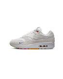 Zijaanzicht van de Air Max 1 met pom pom-details, witte canvas upper en regenboogkleurige buitenzool op een cleane achtergrond