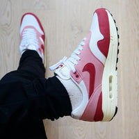 Hielshot van de Nike AM1 Red Stardust met suède hak, geborduurde Nike Air-branding en beige middenzool