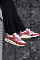 In-hand shot van de Nike Air Max 1 Red Stardust (WMNS) met pastel upper, zichtbare Air-unit en beige accenten