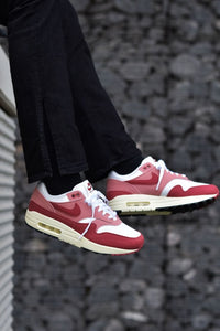 In-hand shot van de Nike Air Max 1 Red Stardust (WMNS) met pastel upper, zichtbare Air-unit en beige accenten
