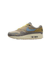 Close-up van de Safari Air Max 1 met grijze safari-panelen en blauwe Swoosh op witte achtergrond, ideaal voor mobile-first sneaker search