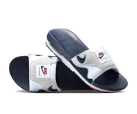 In-hand shot van Air Max 1 Slide Obsidian University Red FJ4007-400 – gestikte strap, iconische zool en retro vibes in navy/white/red