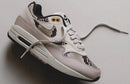 In hand shot van de Nike Air Max 1 Light Orewood Brown met slangenprint textuur, suède toebox en offwhite zool