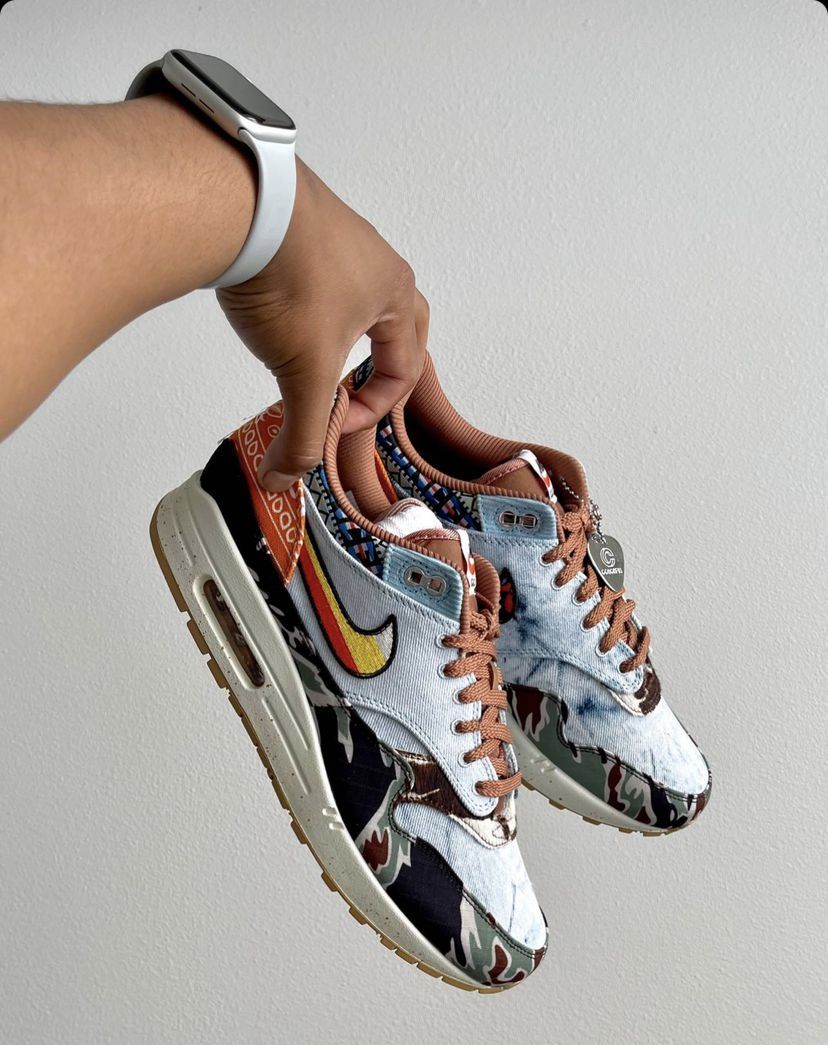 In hand shot van de Concepts Air Max 1 Heavy met zicht op corduroy toebox, flower Swoosh en contrasterende prints – premium afwerking met festival feel