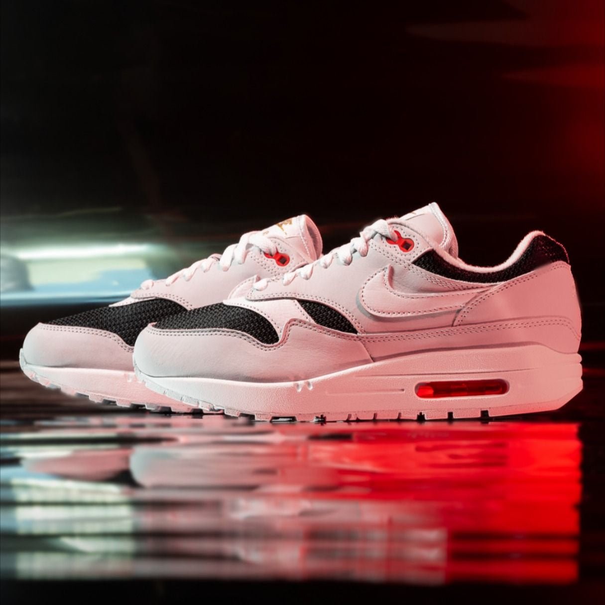 De sneaker gedragen met jeans, gefotografeerd vanaf de zijkant om de klassieke Air Max 1-shape en het rode hielaccent te benadrukken