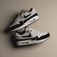 Twee sneakers geflatlayd tegen een beige achtergrond met zachte schaduwen, wat het minimalistische design versterkt