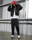 Volledige outfitfoto waarin de sneakers worden gecombineerd met een zwarte bomberjack en rode pet voor een urban look