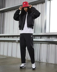 Volledige outfitfoto waarin de sneakers worden gecombineerd met een zwarte bomberjack en rode pet voor een urban look