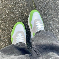 Foto van de Nike Air Max 1 x Patta Chlorophyll gedragen op straat, waarbij de opvallende groene accenten afsteken tegen grijze denim en stedelijk asfalt voor een stijlvolle, dagelijkse look.