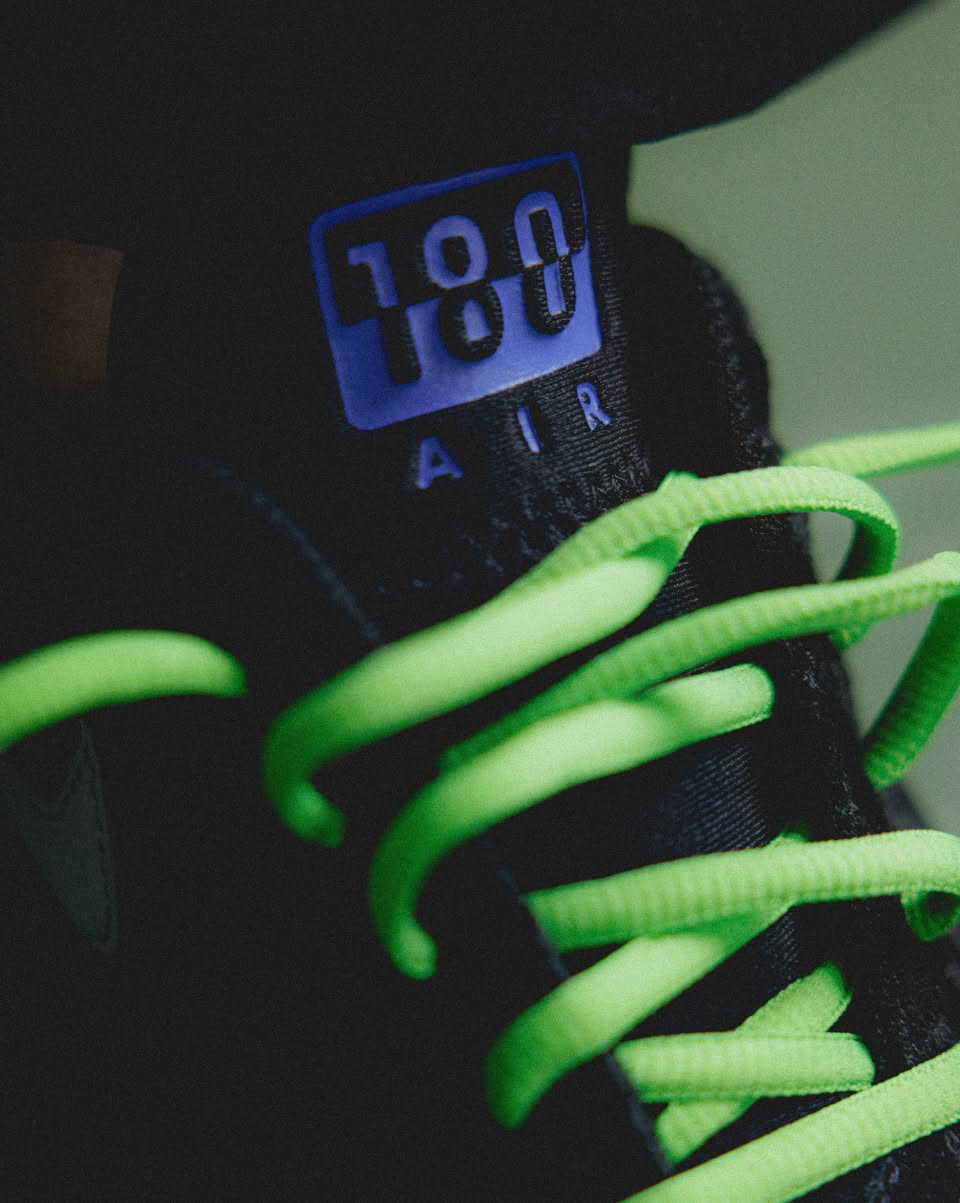 Close-up van de Nike Air Max 180 QS Joker FZ3058-001 met felgroene veters en reflecterende tong, gedetailleerde opname van het Nike Air 180-logo door Snrkickz.