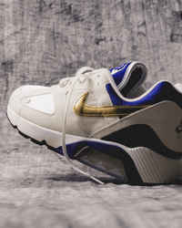 lose-up van de Nike Air Max 180 Summit White Concord FJ9259-101 met zachte leren textuur, witte basis en metallic gouden Swoosh, professioneel gefotografeerd door Snrkickz.
