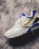 Schuin genomen studiofoto van de Nike Air Max 180 Summit White Concord FJ9259-101 met zichtbare Air unit, gouden Swoosh en contrasterende blauwe hiel, exclusief bij Snrkickz.
