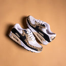 Hangende set Nike Air Max 90 IF1619-100 boven beige ondergrond, luchtige vibe met focus op de lichte buitenzool en print
