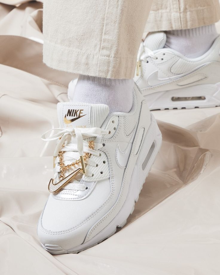 Achteraanzicht van de sneaker met zicht op witte hielstructuur, gestikt Nike-logo en hangende gouden charms

