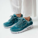 On-feet opname met witte broek, waarbij de glanzende lucky charms en de frisse Ash Green tint duidelijk opvallen