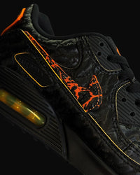 In hand shot van de Nike AM90 QS Volcano met ruwe suède afwerking, zwarte Swoosh en contrasterende gele highlights