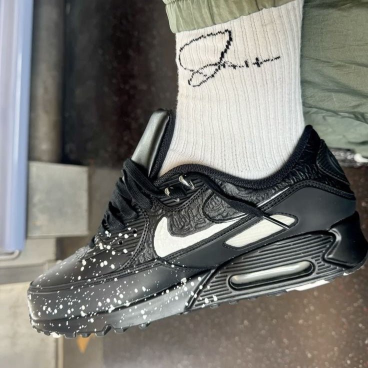 In hand shot van de Nike AM90 Slawn Black met glanzende kunstprint, suède afwerking en zwarte zool