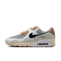 Zijaanzicht van de sneaker met grijze mesh, zwarte swoosh en crème details, tegen een witte achtergrond met oranje gumzool-accenten