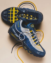 Nike Air Max 95 SB Eric Koston Obsidian Speed Yellow HQ8492-400 met zichtbare veters, donkere zool en contrasterende gele accenten, gefotografeerd in artistieke opstelling voor Snrkickz.