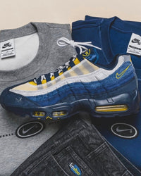 Lifestylefoto van de Nike Air Max 95 SB Eric Koston Obsidian Speed Yellow HQ8492-400 naast skateboard en kleding, casual streetstyle sfeer vastgelegd door Snrkickz.
