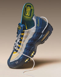 Close-up van de Nike Air Max 95 SB Eric Koston Obsidian Speed Yellow HQ8492-400 met geel stiksel en navy mesh, gefotografeerd in warme studioverlichting voor Snrkickz.