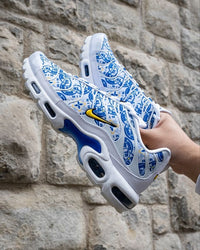 Nike Air Max Plus Lisboa gedragen op straat in zonlicht, vurige kleurencombinatie van rood en geel komt tot leven in een stedelijke setting, streetwear look vastgelegd door Snrkickz.