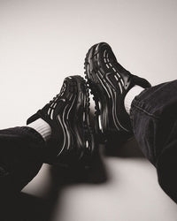Lifestylebeeld van Nike Air Max TL 2.5 Black Metallic Silver op betonnen vloer, beide schoenen diagonaal geplaatst met focus op de zoolconstructie