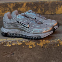 Flatlay van de TL 2.5 Metallic Silver onder goudkleurige straatverlichting, focus op chromen structuur en futuristische belijning