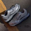 Flatlay van de TL 2.5 Metallic Silver sneaker bij een stoeprand, met metallic upper en zwarte Swoosh in warme belichting