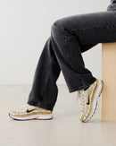 Close-up van de Nike P-6000 Gold Women's IF1787-100 met glanzende gouden overlays, witte mesh textuur en subtiele metallic glans, luxe uitstraling professioneel gefotografeerd door Snrkickz.