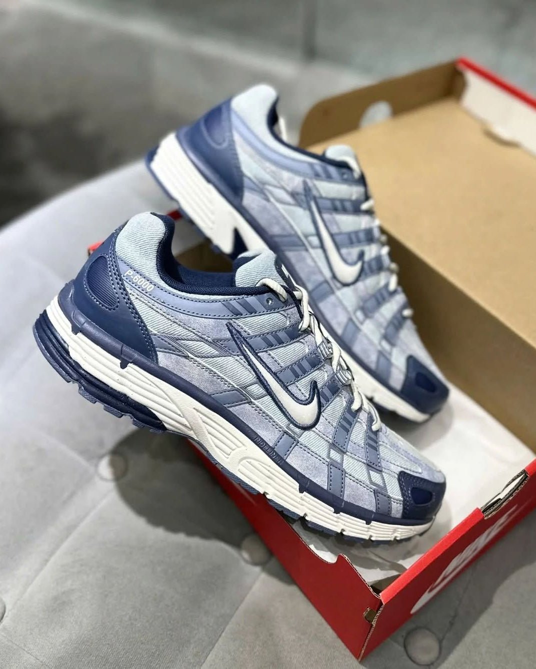 Nike P‑6000 SE Worn Blue Denim – in‑hand shot van sneaker (~330 g), toont lichte denim textuur en gelaagde paneling