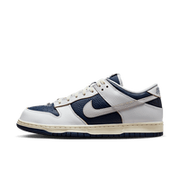 Zijaanzicht van de HUF x Nike SB Dunk Low New York met donkerblauw premium leer, witte toebox en oranje swoosh details