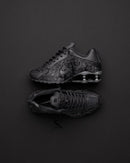 Nike Shox R4 Black Floral op donkere achtergrond, waarbij de floral textuur en reflectie van de zool contrasteren met het licht