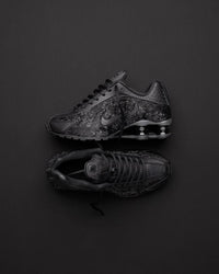 Nike Shox R4 Black Floral op donkere achtergrond, waarbij de floral textuur en reflectie van de zool contrasteren met het licht
