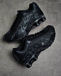 Close-up van de Nike Shox R4 Black Floral met zichtbaar bloemenpatroon, perforaties in de upper en de iconische Shox demping in beweging
