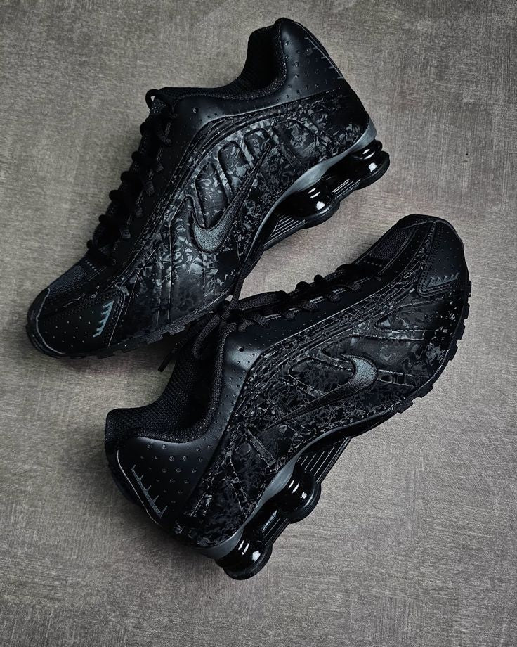 Close-up van de Nike Shox R4 Black Floral met zichtbaar bloemenpatroon, perforaties in de upper en de iconische Shox demping in beweging