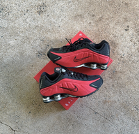Twee Nike Shox R4 sneakers gestyled naast elkaar op ruwe betonnen ondergrond, met focus op rode kleur en reflectie