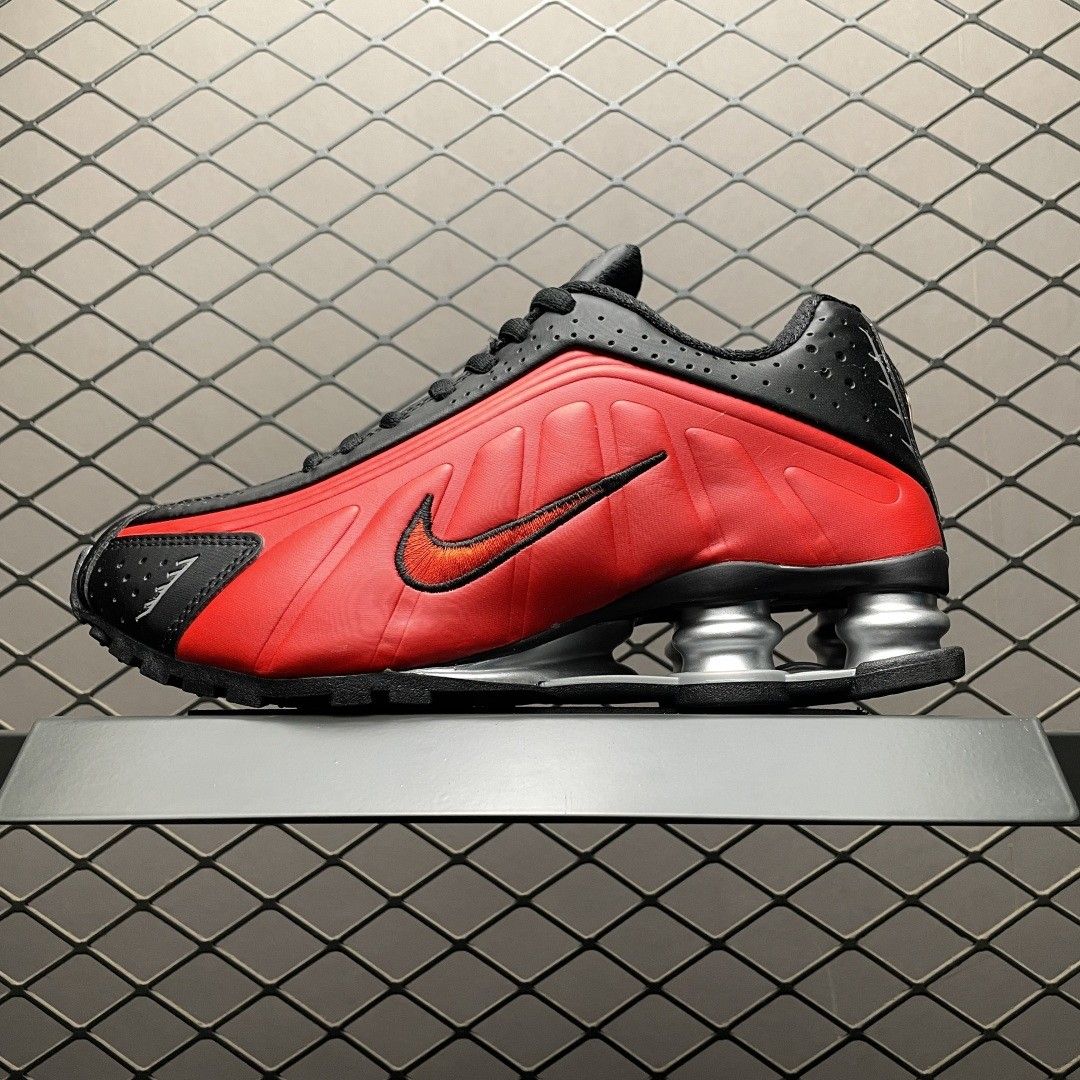 Close-up van de Shox-zool en mesh upper van de University Red R4, gefotografeerd tegen een metalen hek voor urban vibe