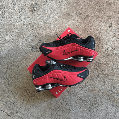 Twee Nike Shox R4 sneakers gestyled naast elkaar op ruwe betonnen ondergrond, met focus op rode kleur en reflectie