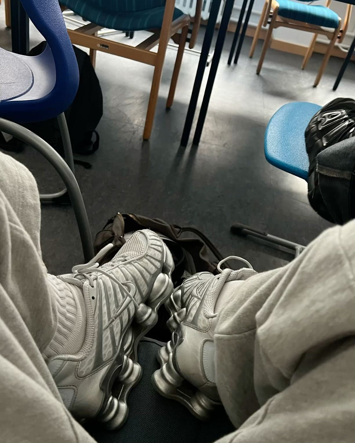 Streetwear-look met Chrome Shox TL aan voeten, benen gestrekt over treinstoel met zilveren details zichtbaar in natuurlijk licht