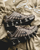 Nike Shox TL Khaki Ironstone Off Noir als paar gefotografeerd liggend op een khaki achtergrond, met nadruk op de earthy kleuren en layered details