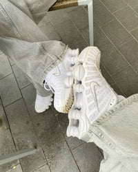 Nike Shox TL Sail aan een touw gehangen, gefotografeerd tegen grijze muur met zicht op reflecterende details en lichte kleurtonen