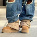 On-foot beeld van UGG Mini Dipper Puffer onder ripped jeans, met focus op dikke zool en volume van het pufferdesign