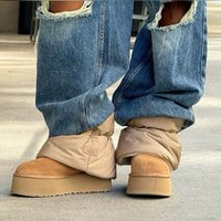 On-foot beeld van UGG Mini Dipper Puffer onder ripped jeans, met focus op dikke zool en volume van het pufferdesign