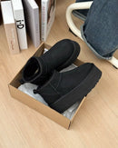 Unboxing moment van de zwarte UGGs in originele verpakking, gefotografeerd boven houten vloer met zicht op binnenvoering