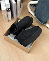 Unboxing moment van de zwarte UGGs in originele verpakking, gefotografeerd boven houten vloer met zicht op binnenvoering